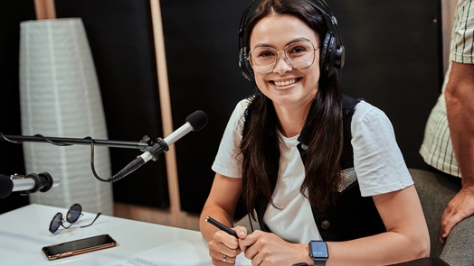 Portrait of happy young female radio host smiling at camera while broadcasting in studio
