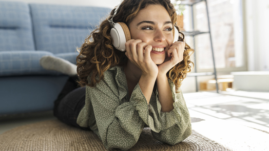 pretty curly-haired woman lying on the floor at home listening to music happy smiling relaxed