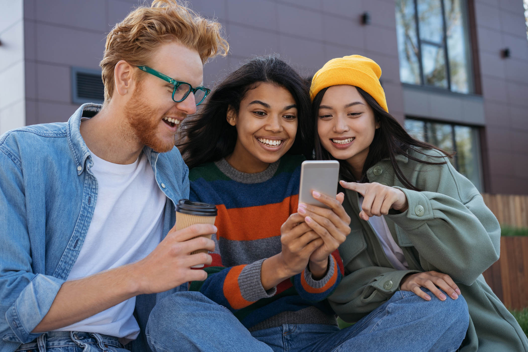 Smiling multiracial friends using mobile phone, watching video, shopping online, having fun outdoors. Young happy students studying, learning language, communication together